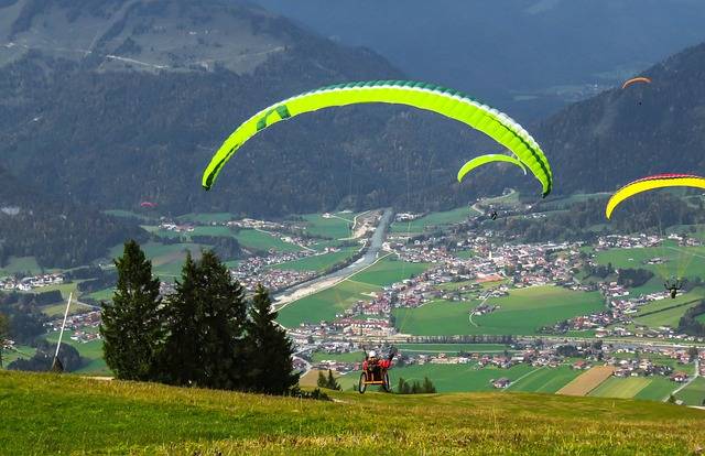 Off-Road Wheelchair for Adventure seekers. A person seated in a wheelchair has just been airborne under a colourful paraglider quite high up in a mountain area. It's a fantastic view, but to me it looks a bit nerve-wracking